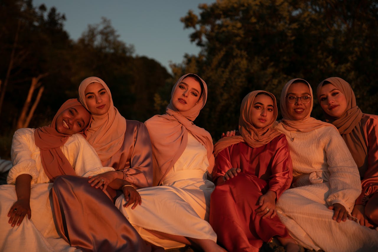 Women in traditional hijabs sit together outdoors in warm sunset light.